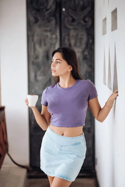 A girl in a stylish denim skirt holds a cup of coffee, a lifestyle.