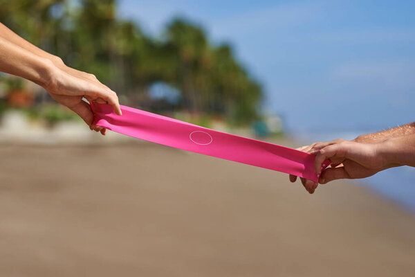 Resistance Bands stretched in the hands of girls on both sides against the backdrop of the sea and palm trees