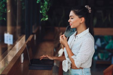 Beyaz tenli, ipek maskeli tatlı bir kız bir internet kafede dizüstü bilgisayarla oturuyor ve çalışıyor..