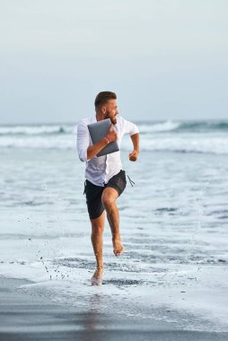 Genç adam sahildeki dalgalardan bir laptoyla öldürüyor.