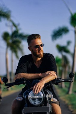 Motosikletli koyu renk elbiseli, gözlüklü genç adam.