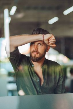 Gömlekli bir Avrupalı, elini cama yaslıyor ve düşünceli görünüyor. Camdan görüntü