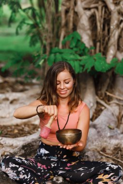 Ağacın yanında oturan bir kız dışarıda müzik kasesinde oynuyor. Yoga ve meditasyon konsepti