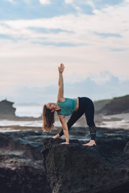 Deniz kenarında yoga yapan bir kız bir ston üzerinde dururken