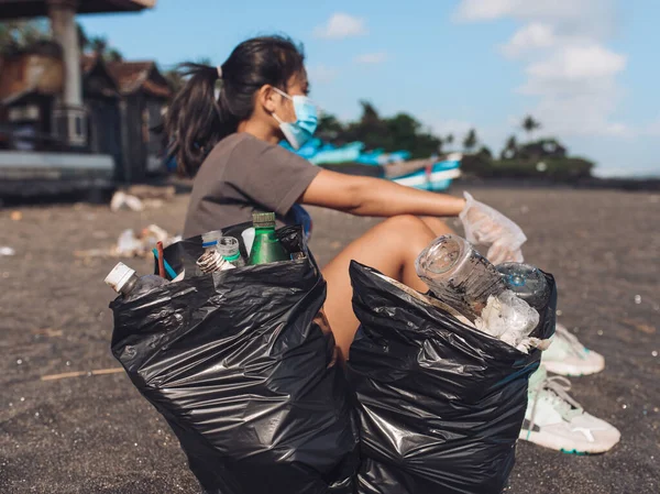 Plajı çöpten temizlemek için iki tane siyah plastik poşet tutan Asyalı kadın. Gönüllü kavramı. Önplana Odaklan - Paket
