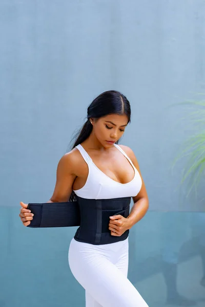 Asian athletic girl wears a slimming belt at home, for fitness. Sweat belt. Exercise preparatio