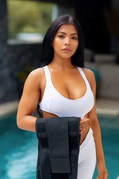 Asian sports girl with a slimming belt on the background of the pool, for fitness. Sweat belt. Exercise preparatio