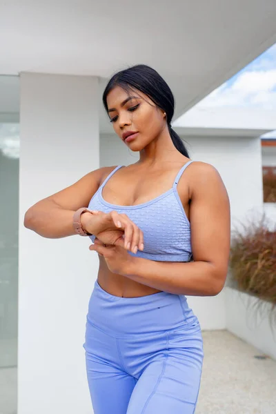 Attractive Asian woman in sportswear is checking the pulse while looking at the clock. Healthy lifestyle in natur