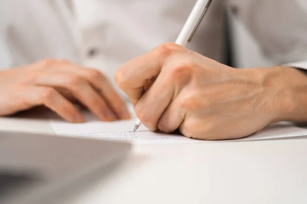 A young businessman makes a report and makes notes on the paper with a pen. Close-up.