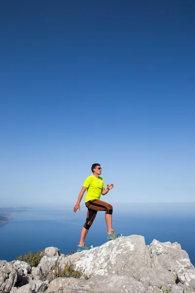 Hombre practicando sendero corriendo con un paisaje costero al fondo — Foto de Stock