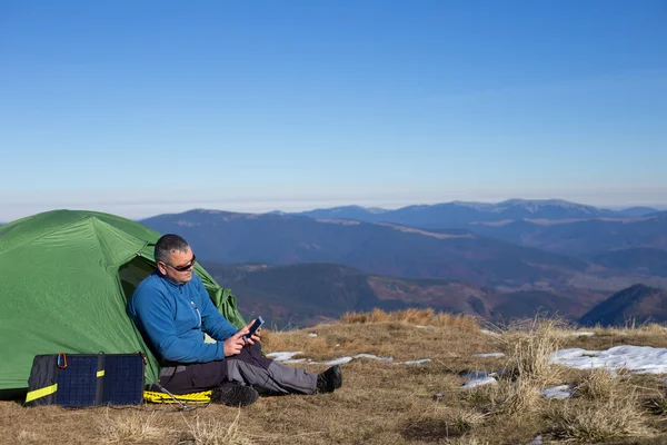 Die Solarzelle, die am Zelt befestigt ist. Der Mann sitzt neben Handyladungen von der Sonne. — Stockfoto