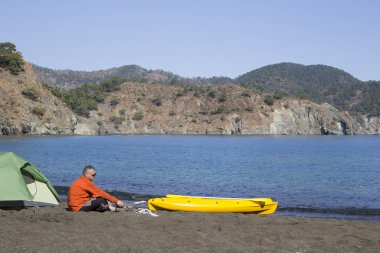 Sahilde bir çadır kampında bir adam oturuyor.