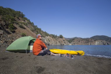 Sahilde bir çadır kampında bir adam oturuyor.