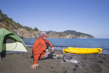 Sahilde bir çadır kampında bir adam oturuyor.