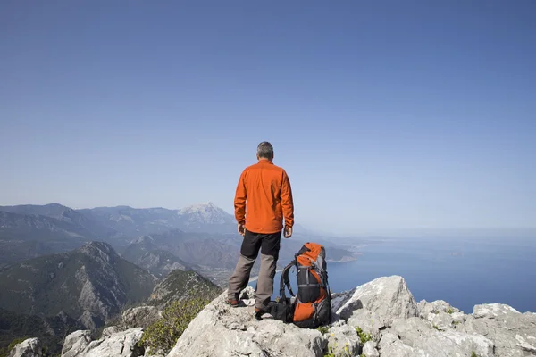 Um viajante fica no topo de uma montanha e olha para o mar . — Fotografia de Stock