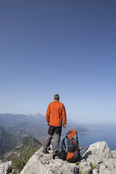 Un viajero se para en la cima de una montaña y mira hacia el mar . — Foto de Stock