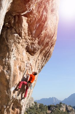 Bir kayaya dağlar karşı atlet tırmanıyor.
