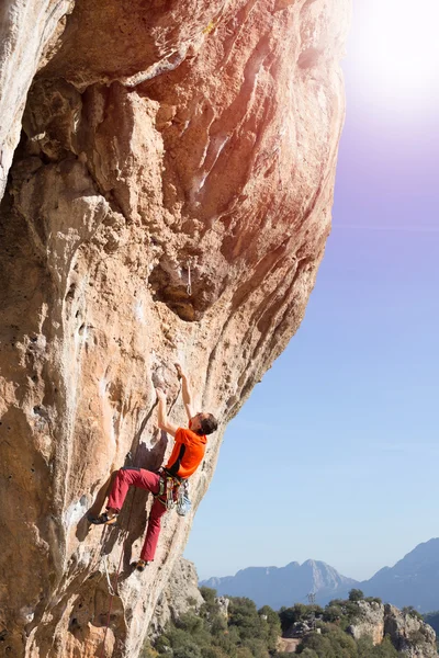 Спортсмен взбирается на скалу против гор . — стоковое фото