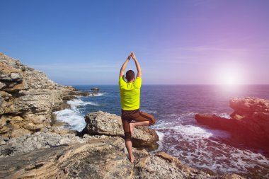 Genç adam plajda yoga yapıyor..