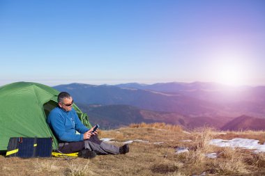 Çadır için bağlı güneş paneli. Güneş'ten cep telefon ücretleri yanında oturan adam.