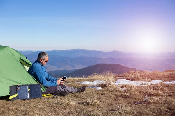 Die Solarzelle, die am Zelt befestigt ist. Der Mann sitzt neben Handyladungen von der Sonne. — Stockfoto