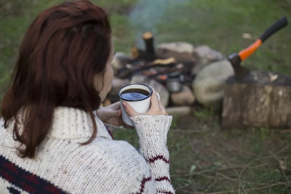 Дівчина сидить біля багаття біля кемпінгу, дивлячись на карту і п'ючи каву . — стокове фото