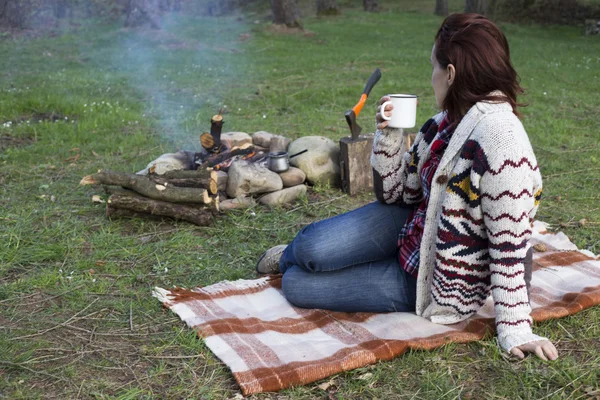 Дівчина сидить біля багаття біля кемпінгу, дивлячись на карту і п'ючи каву . — стокове фото