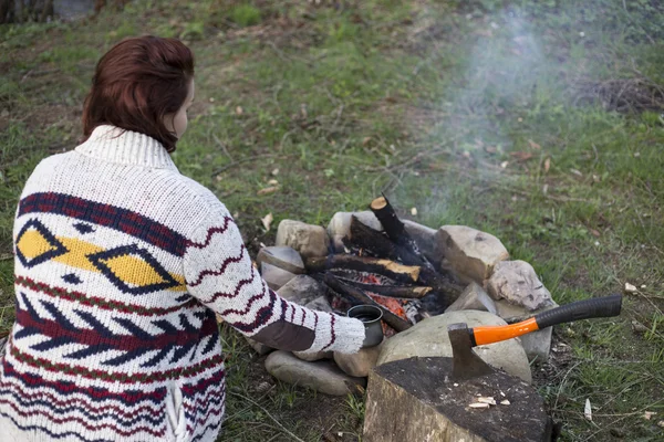 Chica sentada cerca de una fogata en el camping mirando el mapa y tomando café . — Foto de Stock