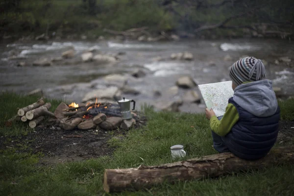 Teenager sitting near a fire in camping and watching map.