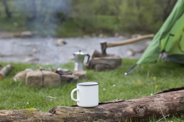 Tazza si trova su un tronco vicino al fuoco in un campeggio . — Foto Stock