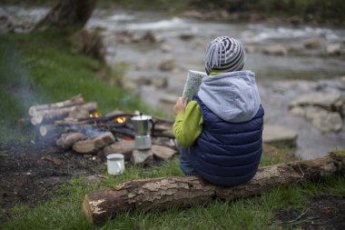 Kamp ve harita izlerken bir ateş yakın oturan genç.