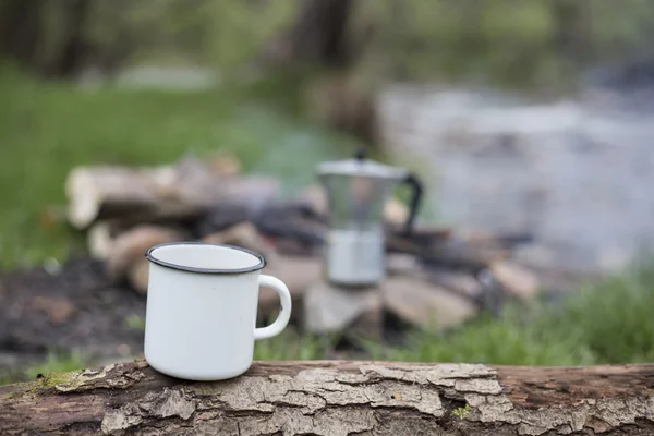 Tazza si trova su un tronco vicino al fuoco in un campeggio . — Foto Stock