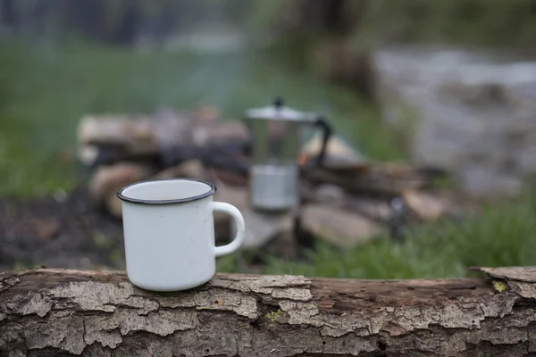 Mug stands on a log near the fire at a campsite. — Stock Photo, Image