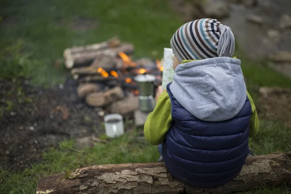 Teenager sitting near a fire in camping and watching map.