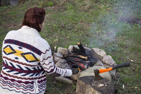 Una chica se sienta junto al fuego y bebe café. . — Foto de Stock