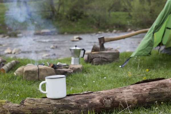 マグカップがキャンプ場で火のそばのログの上に立つ. — ストック写真