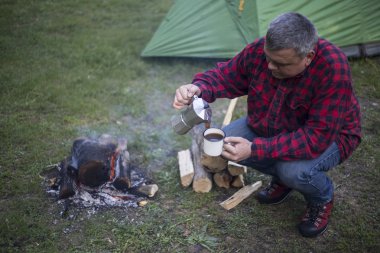 Ateşin yanında kahve içme adam.