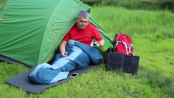 A napelem csatlakozik a sátor. Az ember ül mobiltelefon-díjak a nap. — Stock videók