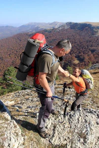 Dağ taş cliff tırmanmaya arkadaşına yardım elini veren adam. — Stok fotoğraf