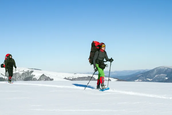 Senderismo de invierno en las montañas en raquetas de nieve con una mochila y tienda de campaña . — Foto de Stock