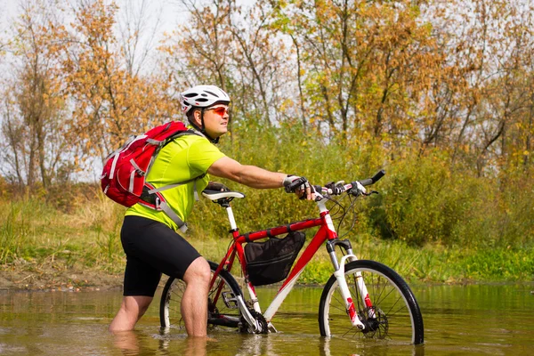 Young athlete crossing rocky terrain with bicycle in his hands. — Stock Photo, Image