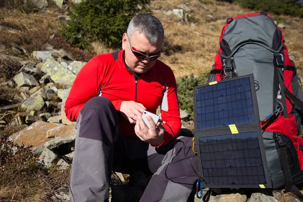 The solar panel attached to the tent. The man sitting next to mobile phone charges from the sun. — Stock Photo, Image