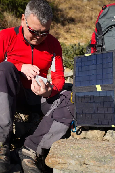 Solpanelen kopplad till tältet. Mannen sitter bredvid mobiltelefon avgifter från solen. — Stockfoto