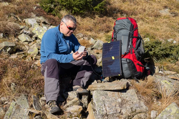 Die Solarzelle, die am Zelt befestigt ist. Der Mann sitzt neben Handyladungen von der Sonne. — Stockfoto