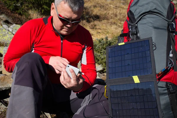 El hombre sentado al lado del teléfono móvil carga desde el sol . — Foto de Stock