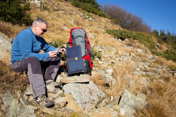 Die Solarzelle, die am Zelt befestigt ist. Der Mann sitzt neben Handyladungen von der Sonne. — Stockfoto