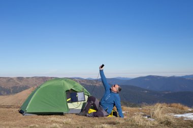 Çadır için bağlı güneş paneli. Güneş'ten cep telefon ücretleri yanında oturan adam.