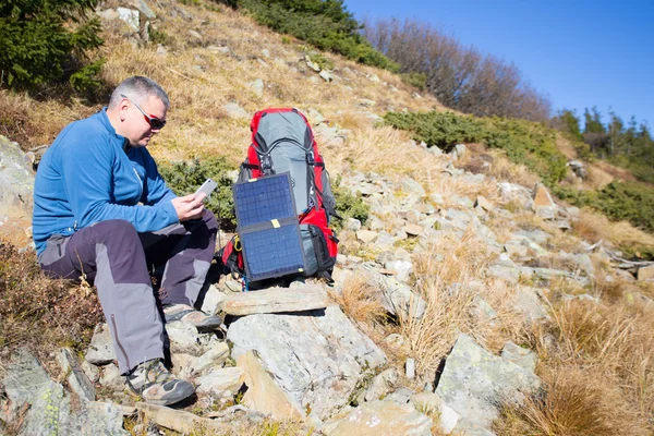 Die Solarzelle, die am Zelt befestigt ist. Der Mann sitzt neben Handyladungen von der Sonne. — Stockfoto