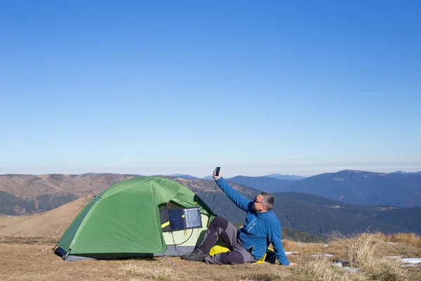 Solpanelen kopplad till tältet. Mannen sitter bredvid mobiltelefon avgifter från solen. — Stockfoto