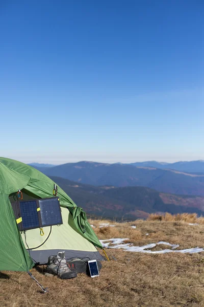 Solpanelen kopplad till tältet. Mannen sitter bredvid mobiltelefon avgifter från solen. — Stockfoto